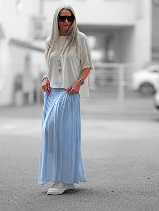 Frau trägt den OFF#DLY Rock Sienna lightblue, einen fließenden Maxirock mit weißem Shirt und Sonnenbrille, im Straßenmode-Stil. Der Rock hat einen weichen Bund und eine elegante Silhouette.