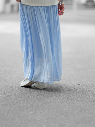Person trägt den OFF#DLY Rock Sienna lightblue, einen fließenden Maxirock mit weichem Bund, kombiniert mit weißen Schuhen. Ideal für elegante und legere Outfits.