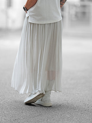 Eine Person trägt den OFF#DLY Rock Sienna lightgrey, kombiniert mit weißen Stiefeln, der Rock fällt elegant in fließendem Material, akzentuiert durch einen weichen Bund für eine feminine Silhouette.