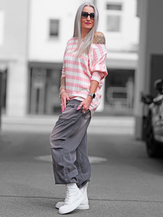 Frau trägt das OFF#DLY Ringel Strick beige/rose, ein gestreiftes Strickshirt mit weicher Rippstruktur, lässigem Schnitt und Rundhalsausschnitt. Perfekt für einen entspannten Frühlingslook.