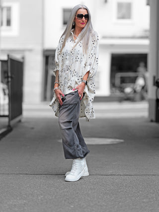 OFF#DLY Longbluse Stick beige black: Frau in weißer Oversize-Longbluse mit schwarzer Stickerei, Hemdblusenkragen und Knopfleiste, trägt Sonnenbrille. Ideal für elegantes und lässiges Styling.