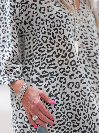 Nahaufnahme eines Modells, das die OFF#DLY Longbluse Leo offwhite trägt, mit einem Leopardenmuster. Zu sehen sind pinke, stilettoförmige Nägel und silberne Schmuckstücke an Hand und Handgelenk.