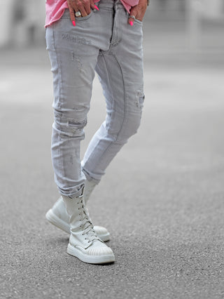 Person trägt OFF#DLY Destroy Denim Zelda lightgrey Jeans mit Destroyed-Details und weißer Stiefel. Nahaufnahme zeigt Hand mit Nagellack, die Tasche zieht. Perfekter urbaner Style.