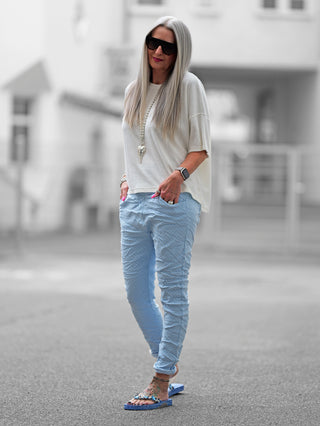 OFF#DLY Pant Lynja lightblue: Frau in hellblauer Crinkle-Hose mit Rautenmuster, kombiniert mit weißem Shirt und Sonnenbrille. Hose mit Bindeband und Taschen, betont modischen und bequemen Stil.