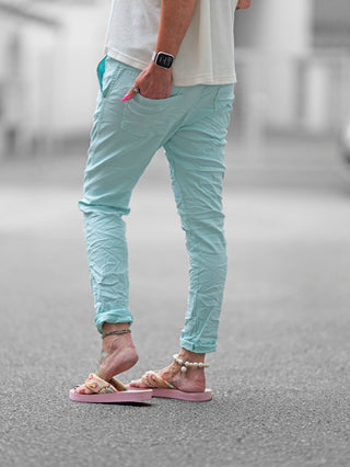 Die OFF#DLY Hose Celeste türkis zeigt einen modernen Crinkle-Look mit asymmetrischem Knopfverschluss und dekorativen Reißverschlüssen, aus stretchigem Material für vielseitige Styling-Optionen.