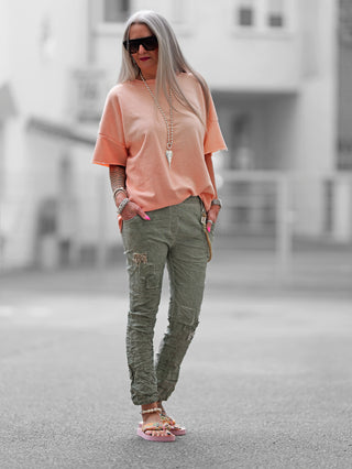 Frau trägt OFF#DLY Pant Vesper khaki mit auffälligen Pailletten- und Stoffpatches, lockerem Schnitt und modischen Kordel-Chain-Elementen, ideal für lässige Anlässe.
