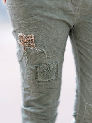 Nahaufnahme der OFF#DLY Pant Vesper khaki, einer Jogpant mit Crinkle-Look und auffälligen Paillettenpatches. Die Hose zeigt stilvolle Kordel-Chain-Elemente an der Gürtelschlaufe und elastischen Bund.
