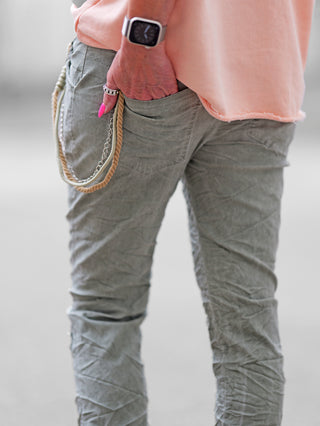 OFF#DLY Pant Vesper khaki: Eine Hand in der Tasche der stylischen Jogpant mit Paillettenpatches und dekorativer Kordel, getragen von einer Person mit Uhr, betont den entspannten, modischen Look.