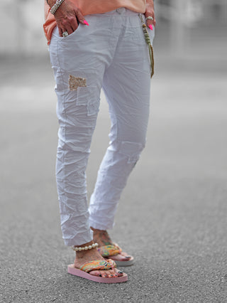 OFF#DLY Pant Vesper white, getragen von einer Person, zeigt weiße Jogpants mit Pailletten- und Stoffpatches, dekorativen Kordel-Chain-Elementen und einem elastischen Bund für lässigen Komfort.