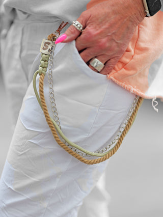 Eine Hand hält die OFF#DLY Pant Vesper white mit Paillettenpatches. Die Jogpant hat einen lässigen Crinkle-Look und dekorative Kordel-Chain-Elemente an der Gürtelschlaufe.