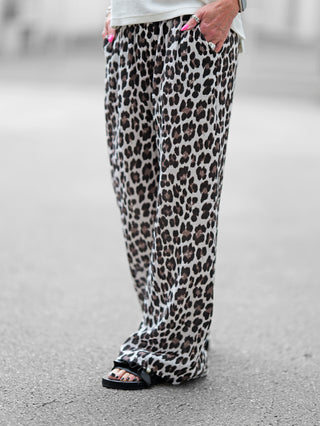 Person trägt OFF#DLY Musselin Pant Leo black/white, weite Musselin-Hose mit Leopardenmuster, elastischem Bund und Kordelzug, sichtbar sind pink lackierte Nägel und ein Ring.