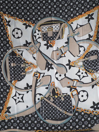 Produktbild des OFF#DLY Tuch Noelia Kette schwarz: Ein schwarz-weißes Stoffmuster mit Taschen, Gürteln und Blumenmotiven, das den modischen und luxuriösen Stil des Schals unterstreicht.