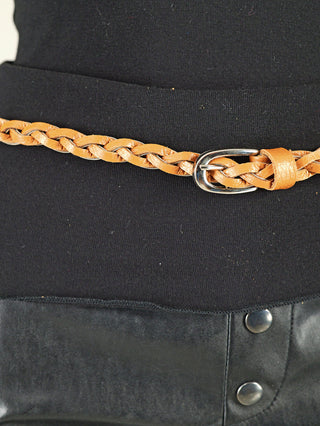 Nahaufnahme des OFF#DLY Flechtgürtels Leder braun mit kleiner silberner Schnalle, getragen über einem schwarzen Oberteil und einer Hose oder Rock mit Druckknöpfen.