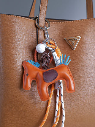 OFF#DLY Taschenanhänger Horse orange, detailreich auf einer Handtasche befestigt, zeigt eine pferdeförmige Form. Naheansicht betont die stilvolle Verarbeitung und das edle Design des Accessoires. Größe ca. 5x15 cm.