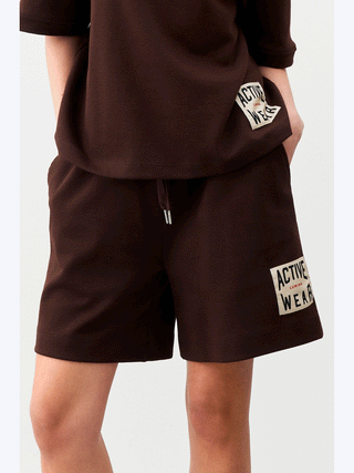 Person trägt Lumina Activ Short mit „Active Wear“-Patch. Lockere Passform, elastischer Bund, ideal für Sport und Freizeit. Sichtbar sind bequeme Shorts mit sportlichem, urbanem Design.