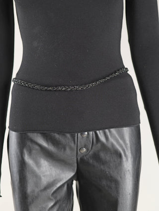 Nahaufnahme des OFF#DLY Zopfgürtel Glitzer black, ein schwarzer Gürtel mit Glitzer-Akzenten und zwei Metallknöpfen, kombiniert mit schwarzer Kleidung. Hergestellt aus Polyester, Glas und Metall.