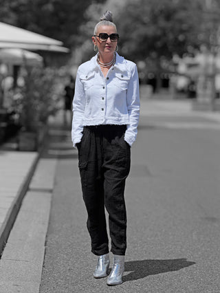 Frau in weißer OFF#DLY Colordenim-Jacke mit ausgefransten Kanten, schwarze Hose, silberne Stiefel. Die Jacke hat ein klassisches Jeansjacken-Design, perfekt für lässige Street-Fashion.