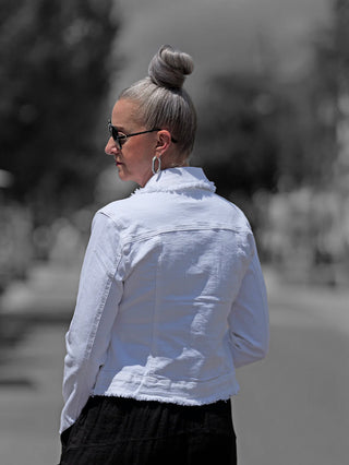 Frau trägt OFF#DLY Colordenim Jacket white mit ausgefransten Kanten, Jeansjacken-Design. Trägt Sonnenbrille, Haare im Dutt.