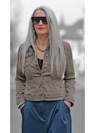Frau mit langen grauen Haaren trägt eine Sonnenbrille und das OFF#DLY Denim Jacket Marrone, eine schmal geschnittene Jacke mit modischem Denim-Stil.