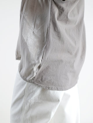Person trägt das OFF#DLY Tee Wake up taupe mit glanzender Vorderseite und goldfarbenem Statement-Print. Kombiniert mit weißen Hosen für einen lässig-eleganten Look.