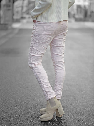Person trägt OFF#DLY Pant Tina rosa, leichte Joggpant mit seitlicher Kettenkordel und Gummibund. Sichtbar sind weiße Stiefel und ein weißer Pullover.