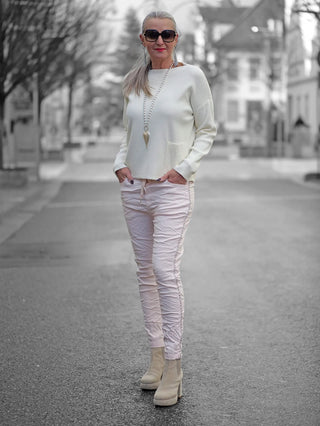 Frau auf der Straße trägt OFF#DLY Pant Tina rosa, eine leichte Joggpant mit Kettenkordel, Gummibund und Taschen, kombiniert mit weißen Stiefeln und Sonnenbrille.