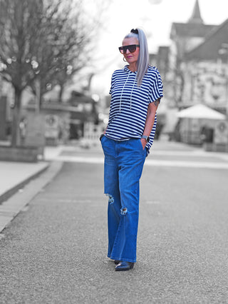 OFF#DLY Ringel m. Kapuze white/blue: Frau trägt gestreiftes Kurzarm-Kapuzenshirt auf der Straße, kombiniert mit blauen Jeans, vermittelt einen lässigen, maritimen Look.