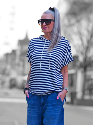 Frau trägt das OFF#DLY Ringel m. Kapuze white/blue Shirt, gestreift mit Kapuze, kombiniert mit Jeans, zeigt lässigen, maritimen Stil. Ideal für entspannte, sportliche Looks.