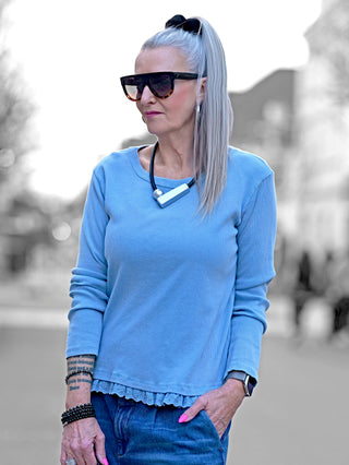 Frau mit grauem Haar trägt OFF#DLY Ripp Longsleeve lightblue, erkennbar an der feinen Rippenstruktur und Spitzendetail am Saum. Kombiniert mit Jeans, ideal für Übergangstage.