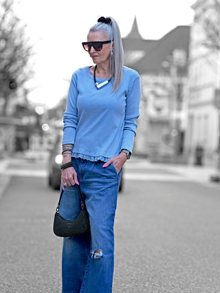 Frau trägt das OFF#DLY Ripp Longsleeve lightblue, ein hellblaues Baumwollshirt mit Rippenstruktur und Spitzendetail, kombiniert mit Jeans und Sonnenbrille, während sie auf der Straße geht.