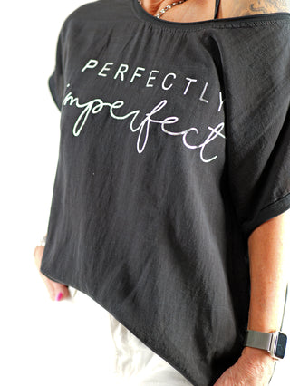 Person trägt das OFF#DLY Tee Perfectly black, ein locker geschnittenes Oversize-T-Shirt mit großem Frontprint Perfectly imperfect, kombiniert mit einem besonderen Materialmix für hohen Tragekomfort.
