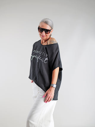 Frau trägt das OFF#DLY Tee Perfectly black, ein oversized schwarzes T-Shirt mit großem Perfectly imperfect-Frontprint, kombiniert mit lässiger Eleganz und hochwertigem Materialmix. Ideal für selbstbewusste Modefans.