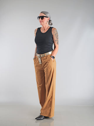 Frau mit Tattoos trägt das OFF#DLY Top Neve black, ein lässiges Baumwoll-Top mit Smiley-Patch, kombiniert mit einem Gürtel und Sonnenbrille. Perfekt für Freizeit oder Urlaub.