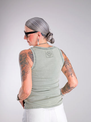 OFF#DLY Top Neve khaki, ein lässiges Baumwoll-Top mit Smiley-Patch, präsentiert an einer tätowierten Frau. Perfekte Passform bis Größe 40, ideal für sommerliche Outfits.