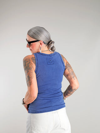 OFF#DLY Top Neve marine: Frau trägt ärmelloses Baumwoll-Top mit Smiley-Patch, sichtbare Tattoos an den Armen, stilvolles Design, ideal für sommerliche Outfits, perfekt kombinierbar mit Jeans oder Röcken.