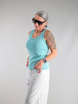 Frau mit Tattoos trägt das OFF#DLY Top Neve türkis, ein lässiges Baumwoll-Top mit Smiley-Patch, sportlichem Rundhalsausschnitt und perfekter Passform, ideal für Sommeroutfits.