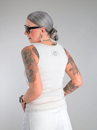 OFF#DLY Top Neve sand: Frau mit Tätowierungen trägt lässiges Baumwoll-Top mit Smiley-Patch, sportlichem Rundhalsausschnitt und schmaler Passform. Ideal für Sommeroutfits.