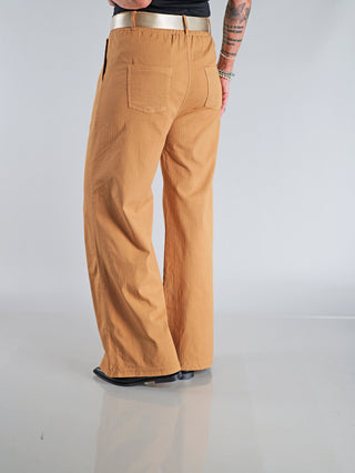 Person trägt OFF#DLY Wide Leg Pant Rina camel mit weitem Bein und elastischem Bund. Ein markanter Glanzgürtel ergänzt das Design. Ideale Passform für stilvolle Eleganz und Komfort.