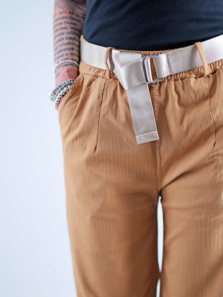 OFF#DLY Wide Leg Pant Rina camel, getragen mit einem markanten Glanzgürtel. Die Hose hat ein weites Bein und einen elastischen Bund, betont durch Seitentaschen und fließenden Stoff.