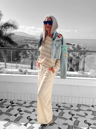 Frau vor Fenster in OFF#DLY Wide Leg Pant Rina creme mit weitem Bein und elastischem Bund, ergänzt durch markanten Glanzgürtel. Ideal für vielseitige, stilvolle Outfits.