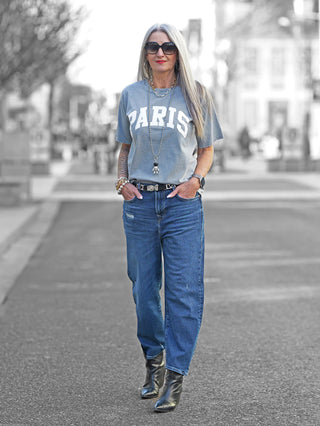 Frau trägt Off#DLY Tee paris grey mit Rundhals und PARIS-Print, kombiniert mit Jeans. Das Shirt passt bis Größe 40 und hat eine gerade Passform.