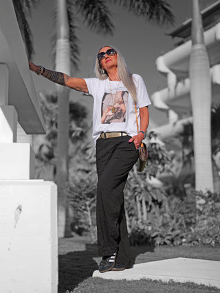 Frau im Freien trägt das OFF#DLY Tee champagne white mit „Champagne Problems“-Frontprint und Glitzersteinen, kombiniert mit schwarzer Hose, goldener Kette und Sonnenbrille.