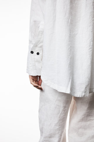 Thom Krom Bluse WH18 offwhite: Person trägt ein oversized Leinen-Langarmhemd mit langen Manschetten und abgerundetem Saum. Nahaufnahme zeigt weiße Knöpfe und weiches Baumwoll-/Leinenmaterial.