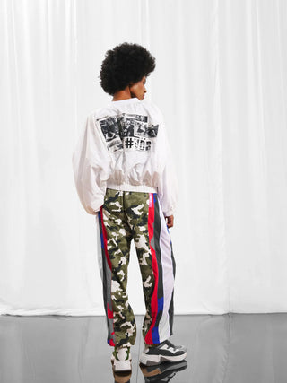 #VDR Bomberjacke white: Frau in weißer Bomberjacke mit Collage-Print auf dem Rücken, kombiniert zu Tarnhosen und Sneakers, zeigt urbanen Stil. Kurzer Schnitt mit elastischen Bündchen und #VDR-Schriftzug am Ärmel.