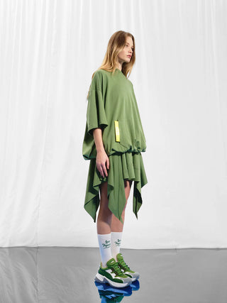 Frau trägt #VDR Sweater oliv, Oversize-Schnitt mit Kapuze, asymmetrischem Saum und auffälligem Pailletten-Backprint, kombiniert mit grünen und weißen Sneakers, für urbanen Streetstyle.