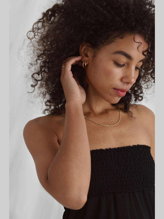 Frau mit lockigem Haar trägt das Cotton Candy Nica Top black, ein schwarzes, trägerloses Top mit gesmoktem Bund und Seitenschlitzen, passend für einen eleganten, modischen Look.