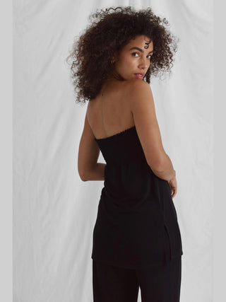 Frau in einem schwarzen Cotton Candy Nica Top, mit gesmoktem Bund und Seitenschlitzen, posierend im Fotostudio. Das Top zeigt eine reguläre Passform und bietet hohen Tragekomfort.