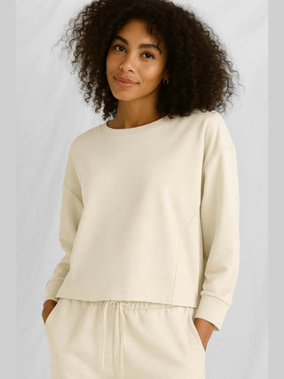 Eine Frau trägt das Cotton Candy Tee Nora offwhite, ein lässiges Langarmshirt mit Rundhalsausschnitt und offenen Kanten, ideal für einen entspannten Look.