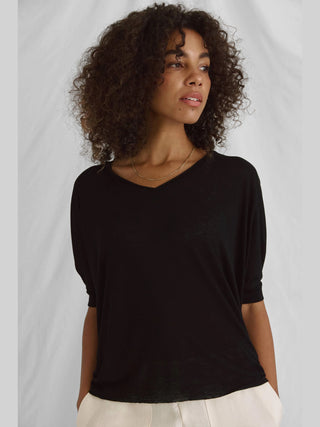Frau mit lockigem Haar trägt das Cotton Candy Tee Helay black, ein schwarzes, oversized T-Shirt mit V-Ausschnitt und Saumversatz, kombiniert mit einer goldenen Kette.