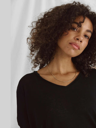 Frau mit lockigem Haar trägt das Cotton Candy Tee Helay in Schwarz, ein oversized Shirt mit V-Ausschnitt aus Viskose-Polyester-Mix, sichtbar angenehm und weich.